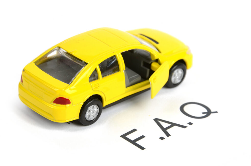 A small yellow toy car with an open door is placed on a white surface next to the letters "F.A.Q." written in black.